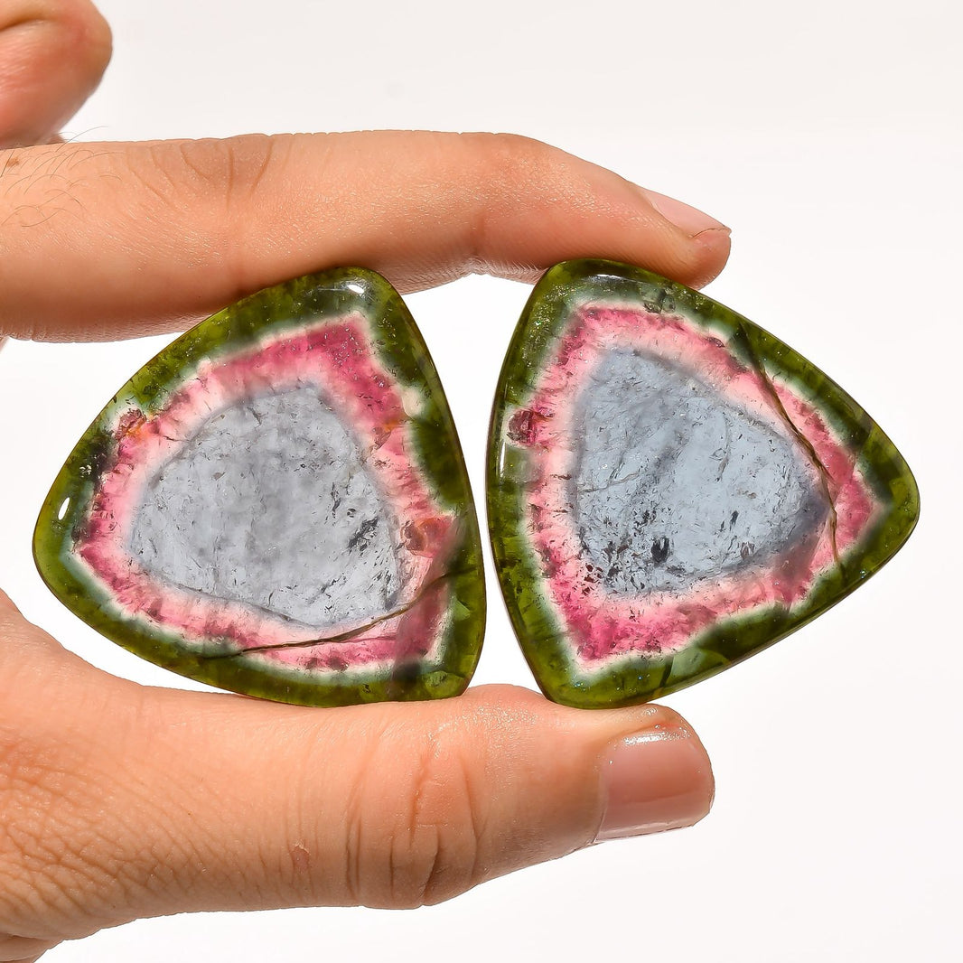 Two green stone earrings with a gray center held between fingers against a white background
