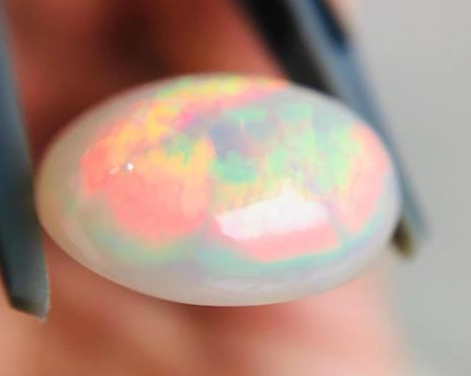 Close-up of a colorful opal stone held between fingers.