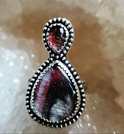 Silver ring with a teardrop design featuring a butterfly and red stone on a textured background.