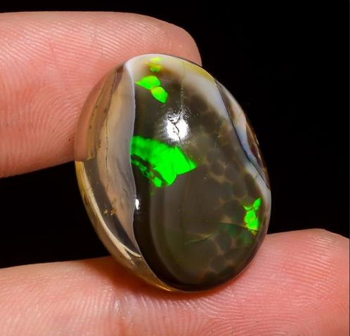 Close-up of a glowing green opal held between fingers.